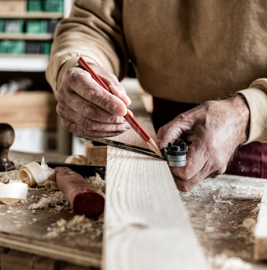 Carpenter making measurements with a pencil and a metal ruler on wooden plank